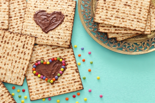 Pieces of matzah on a platter and scattered on a teal surface and topped with chocolate hearts